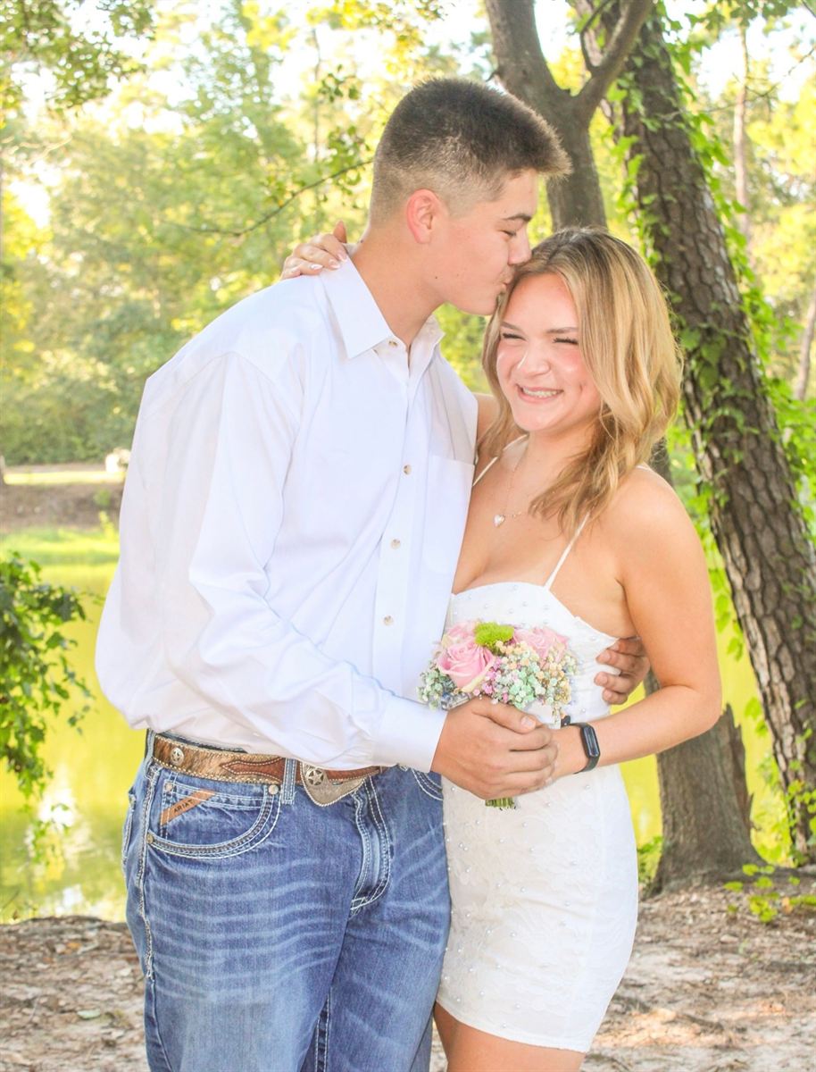 Homecoming couple sharing a kiss on the cheek among trees