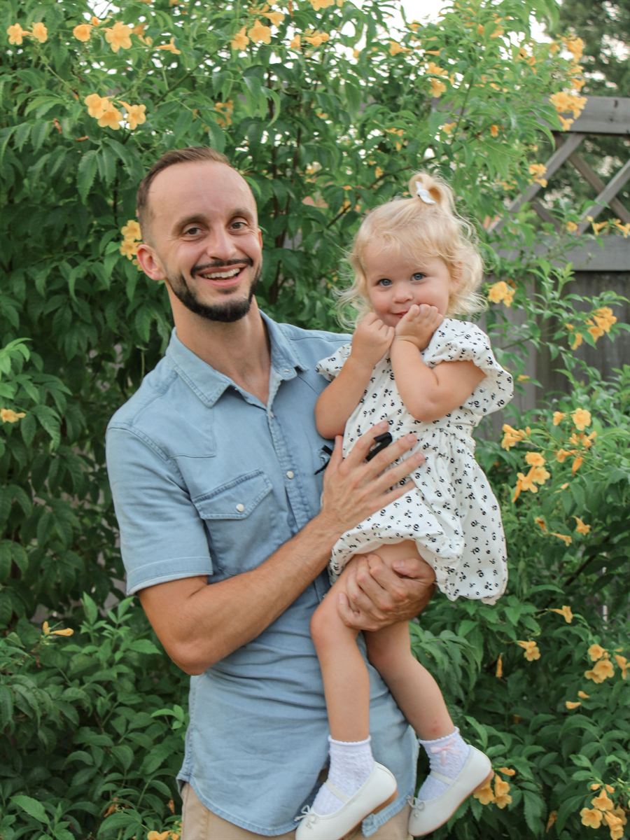 Smiling dad holding his toddler daughter among flowering bushes