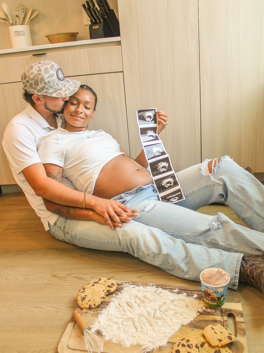 Expecting parents relaxing on the kitchen floor holding ultrasound photos